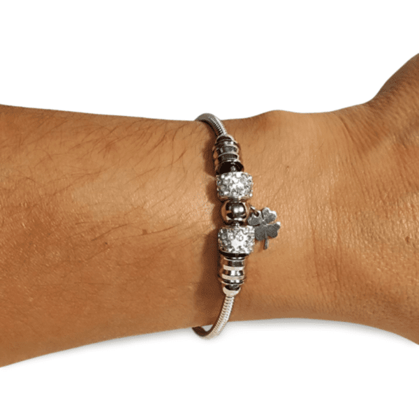 Pulsera rígida de acero inoxidable plateada con circonitas y charm de trébol en la muñeca