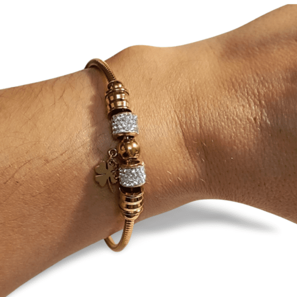 Pulsera rígida dorada de acero inoxidable con circonitas y charm de trébol en la muñeca