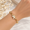 Pulsera dorada con mariposa blanca nacarada y detalles brillantes puesta en la muñeca