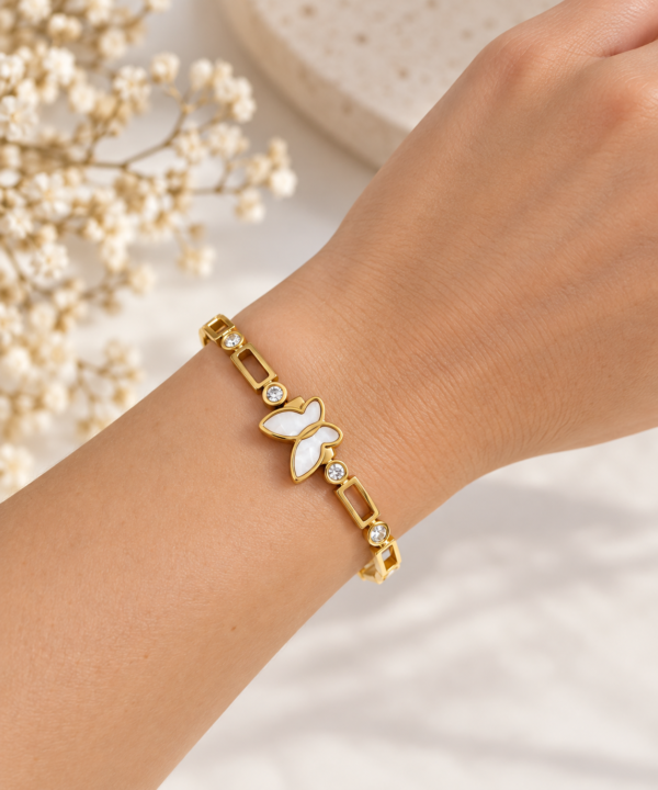 Pulsera dorada con mariposa blanca nacarada y detalles brillantes puesta en la muñeca
