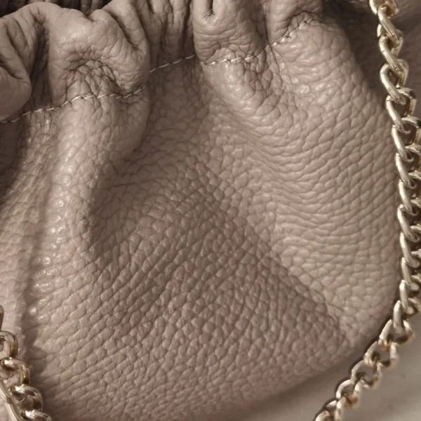 Detalle del frunce del bolso de piel ERYNA Detalle del fruncido y la piel granulada del bolso rosa nude con cadena dorada