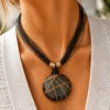 Collar ERYNA colgante circular envuelto en acero con modelo Modelo con collar ERYNA de cordones negros finos y gran colgante circular de piedra envuelto en hilo de acero dorado