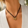 Collar ERYNA corazón dorado con cinta textil puesto Mujer con collar ERYNA de cinta textil oscura y colgante de corazón dorado martillado
