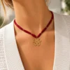 Collar ERYNA flor dorada con cinta textil puesto Mujer con collar ERYNA de cinta textil roja y colgante de flor dorada calada