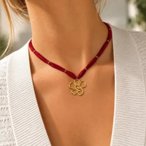 Collar ERYNA flor dorada con cinta textil puesto Mujer con collar ERYNA de cinta textil roja y colgante de flor dorada calada