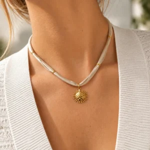Mujer con collar ERYNA de cinta textil beige y colgante de sol dorado en relieve