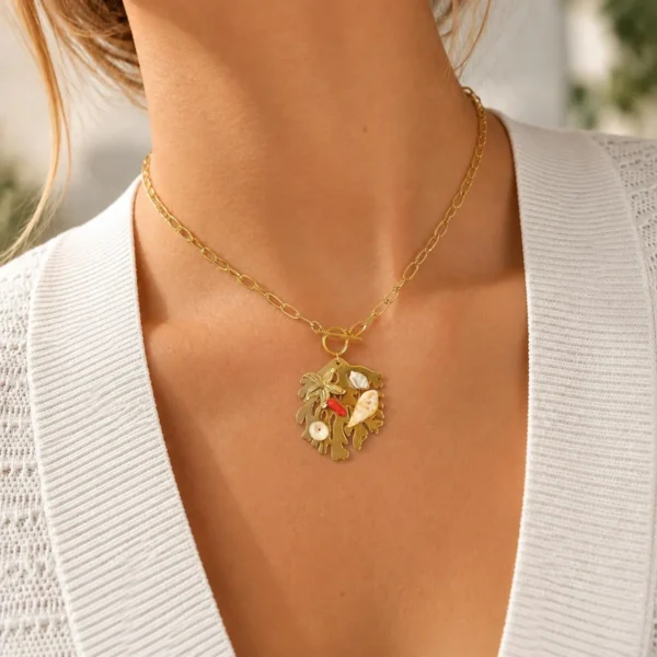 Mujer con collar dorado con colgante de hojas doradas, concha, coral rojo y perlas