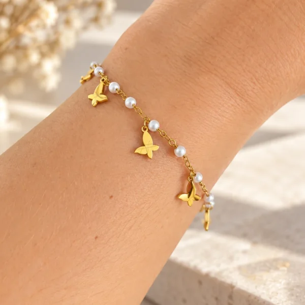 Muñeca con pulsera dorada de perlas y mariposas colgantes en acero inoxidable ERYNA